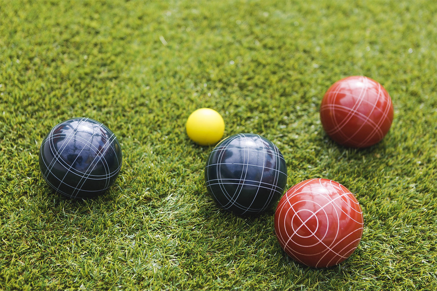 Red, yellow and black bocce balls rest on the grass.